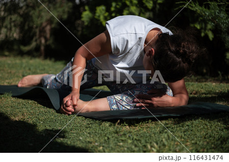 Woman practicing yoga outdoors on a sunny day in a lush garden, stretching and focusing on relaxation and flexibility 116431474