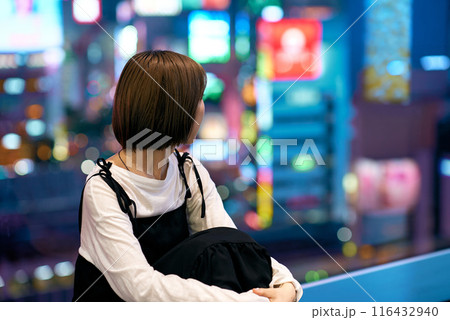 夜の繁華街を見つめる若い女性 116432940