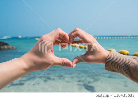 Couple two hands forming and making heart shape gesture on the beach Couple two hands forming and making heart shape gesture on the beach 116433033