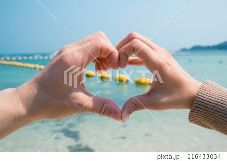 Couple two hands forming and making heart shape gesture on the beach 116433034