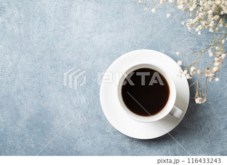 a spring bouquet with white gypsophila flowers over a cup of black coffee on a blue  table.  116433243