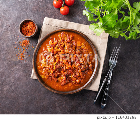 Stewed oxtails with vegetables in a wooden plate on a dark background with fresh tomatoes and herbs. 116433268