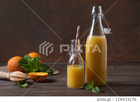 freshly squeezed orange juice in two bottles with citrus fruits on a brown wooden background. 116433276