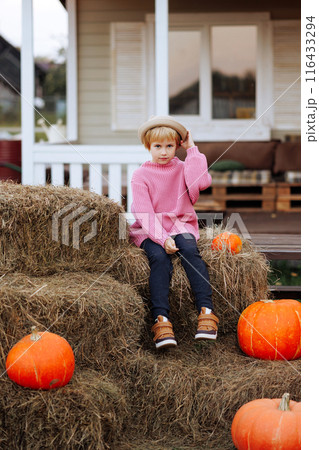 A young girl sits on hay bales in front of pumpkins. 116433294