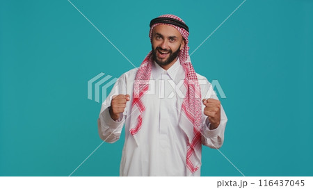 Modern guy cheering and showing his support in front of camera, feeling optimistic and joyful about something. Middle eastern person being brave and giving strength with cheers. 116437045