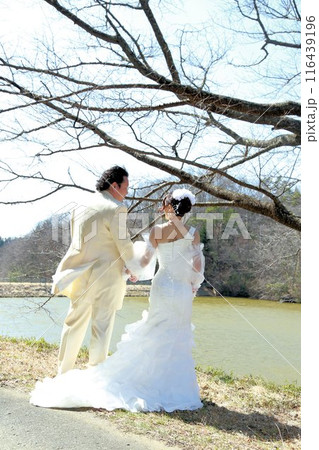 ウエディングドレス姿の新婦様とタキシード姿の新郎様フォトウエディング後ろ姿、湖畔でロケーション撮影 116439196