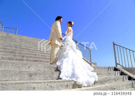 ウエディングドレス姿の新婦様とタキシード姿の新郎様フォトウエディング青空の美しい海ロケーション撮影 116439348