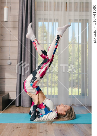 Woman Doing Inverted Yoga Pose on Blue Mat in Home Studio 116441080