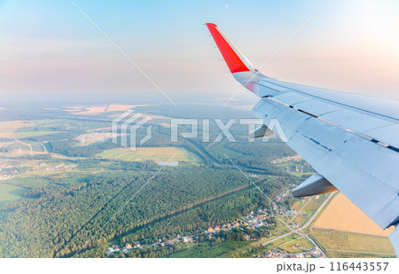 View of airplane wing, blue skies and green land during landing. Airplane window view. 116443557