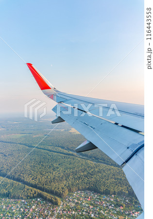 View of airplane wing, blue skies and green land during landing. Airplane window view. 116443558