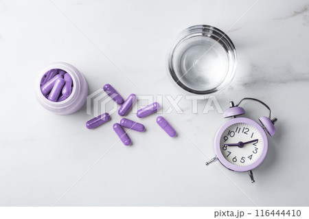 Sleeping pills concept, purple capsules and bottle, glass of water and alarm clock on white table, top view Sleeping pills concept, purple capsules and bottle, glass of water and alarm clock on white table, top view 116444410