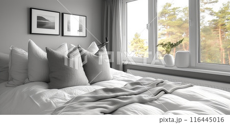 Bedroom with a white bed and a window. The bed is covered with grey and white pillows and a blanket. There are two mock up pictures on the wall 116445016