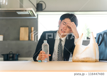 帰宅後ダイニングで悩むスーツ姿のアジア人ビジネスマン（頭痛・疲労・過労・離婚） 116447480
