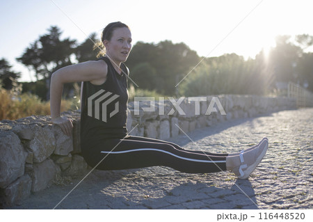 A woman is doing a push up on a stone wall 116448520