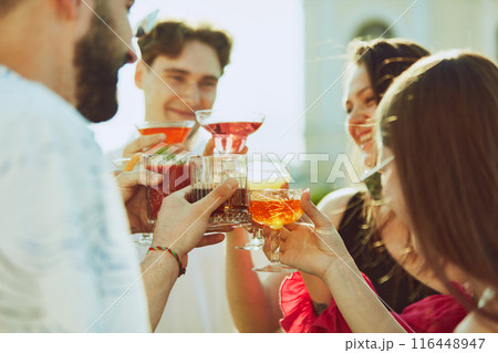Golden light of sun enhances cheerful toast among friends, their drinks shimmering. Party. Golden light of sun enhances cheerful toast among friends, their drinks shimmering. Party. 116448947
