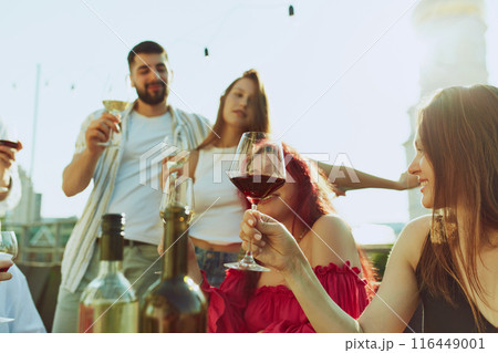 Laughter and cheers fill air as friends come together for toast, illuminated by golden sunlight at party outdoor. Laughter and cheers fill air as friends come together for toast, illuminated by golden sunlight at party outdoor. 116449001