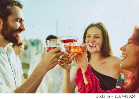 Group portrait of young adults gathers for festive toast, on party and their drinks glowing in radiant sunlight. 116449024