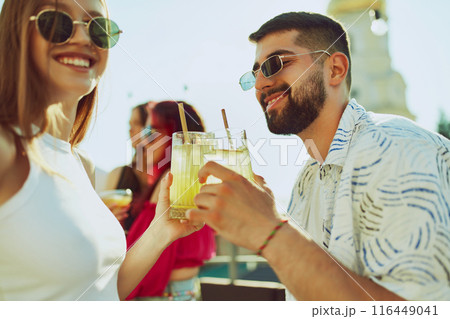 Lively outdoor gathering features friends toasting with colorful cocktails, enjoying each other's company. 116449041