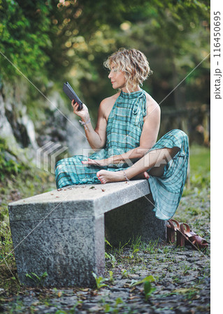 Woman reads from ebook on bench Woman reads from ebook on bench 116450695