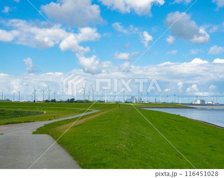 Groningen, Netherlands - August 9th 2023: View over a dyke towards industrial areas in the Ems mouth region 116451028