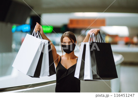 Young woman in protective black medical mask on her face with shopping bags in the mall.Covid-2019. Young woman in protective black medical mask on her face with shopping bags in the mall.Covid-2019. 116451247