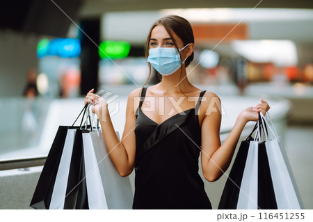 Fashionable woman in protective medical mask with shopping bags walking in the mall. Covid-19. Fashionable woman in protective medical mask with shopping bags walking in the mall. Covid-19. 116451255