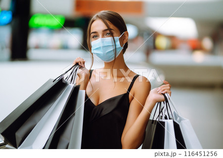 Fashionable woman in protective medical mask with shopping bags walking in the mall. Covid-19. Fashionable woman in protective medical mask with shopping bags walking in the mall. Covid-19. 116451256