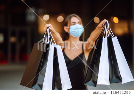 Fashionable woman in protective medical mask with shopping bags walking near mall. Covid-19. 116451299