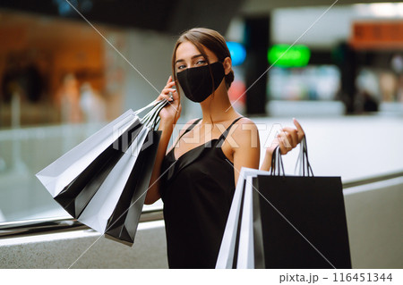 Young woman in protective black medical mask on her face with shopping bags in the mall.Covid-2019. Young woman in protective black medical mask on her face with shopping bags in the mall.Covid-2019. 116451344