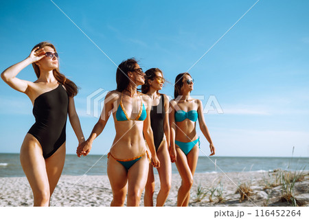 Happy four girls strolling along a beach. Young women enjoying on beach holiday. Summer, relax. 116452264