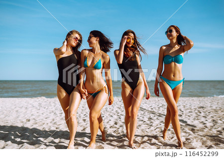 Happy four girls strolling along a beach. Young women enjoying on beach holiday. Summer, relax. 116452299