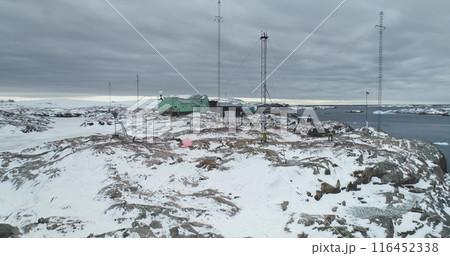Snow covered Antarctica rocky coast island, aerial view Vernadsky science base polar station. Antarctic expeditions and travel, exploration. People explore South Pole wild nature. Aerial drone flight 116452338