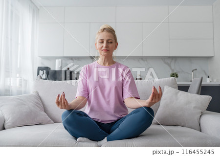 Elderly lady does yoga on the sofa in modern living room, enhancing mental and physical wellbeing Elderly lady does yoga on the sofa in modern living room, enhancing mental and physical wellbeing 116455245