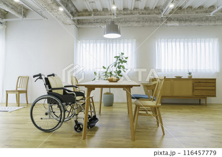 明るい窓のあるリビングルームに置かれた車椅子 116457779