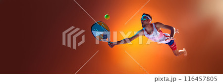 Competitive man playing beach tennis, in motion hitting ball with racket against orange studio background in neon light Competitive man playing beach tennis, in motion hitting ball with racket against orange studio background in neon light 116457805