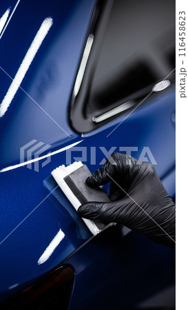 Image shows a person applying a ceramic coating to the surface of a blue car 116458623