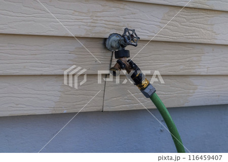 Green garden hose reel on wall for water the plants in front yard. Green garden hose reel on wall for water the plants in front yard. 116459407