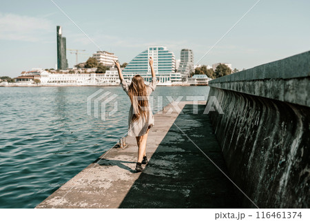woman in a white dress is walking on a pier near the water. The scene is peaceful and serene, with the woman's long hair blowing in the wind. 116461374