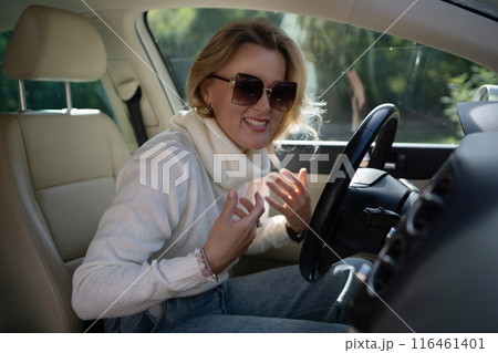A blonde woman in a white sweater and jeans is driving. Happy woman sitting in a car with a white interior. 116461401