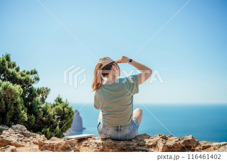 A woman is sitting on a rock overlooking the ocean 116461402