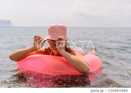 A woman is laying on a pink inflatable raft in the ocean. The scene is peaceful and relaxing, with the woman enjoying the water and the sun. A woman is laying on a pink inflatable raft in the ocean. The scene is peaceful and relaxing, with the woman enjoying the water and the sun. 116461460