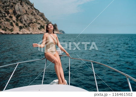 Yacht woman in bikini posing while on the bow of a yacht. Happy woman is sunbathing on the bow of a ship during a boat trip. Travel concept, vacation at sea 116461502