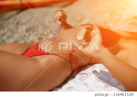 Woman taking red bikini off on beach for tan, lady stripping holiday swimsuit with bow in string. Fun and relax, sexy model untying swimming costume bra, happy woman in swimwear on vacation 116461520