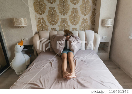 A girl is laying on a bed with pillows and a stuffed duck. She is looking at the camera with a sad expression. 116461542