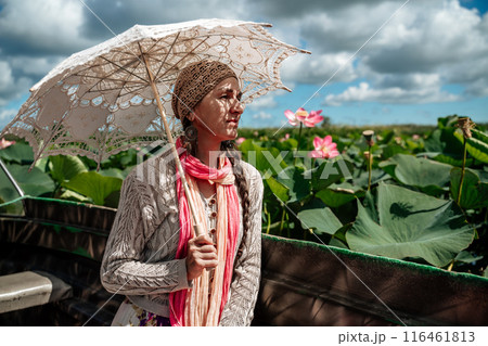 A woman wearing a hat and holding an umbrella is looking at a field of pink flowers. The scene is peaceful and serene, with the woman taking in the beauty of the flowers. A woman wearing a hat and holding an umbrella is looking at a field of pink flowers. The scene is peaceful and serene, with the woman taking in the beauty of the flowers. 116461813