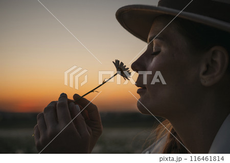 A woman is holding a flower and smelling it. The image has a peaceful and calming mood, as the woman is enjoying the simple pleasure of smelling the flower. A woman is holding a flower and smelling it. The image has a peaceful and calming mood, as the woman is enjoying the simple pleasure of smelling the flower. 116461814