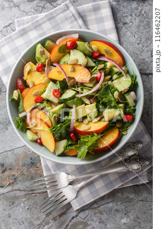 Homemade salad with nectarine, avocado, cucumber, red onion, chili, arugula, spinach and pumpkin seeds close-up in a bowl on the table. Vertical top view 116462207
