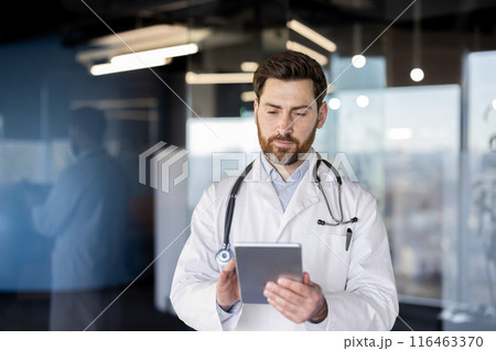 Focused doctor using a digital tablet in modern hospital office. Medical professional reviewing patient information, conducting research, or managing healthcare tasks. Technology healthcare setting. 116463370