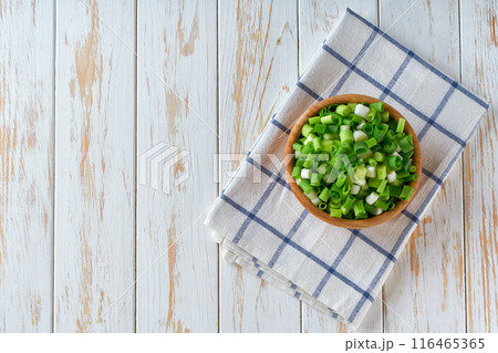 Chopped green onion in a wooden bowl on a white table .Top view. 116465365