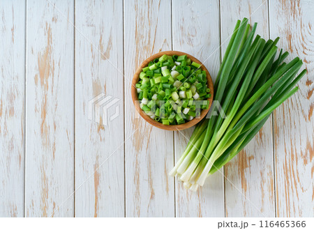 Chopped spring onions in a wooden bowl on a white table . Copy space for text. 116465366